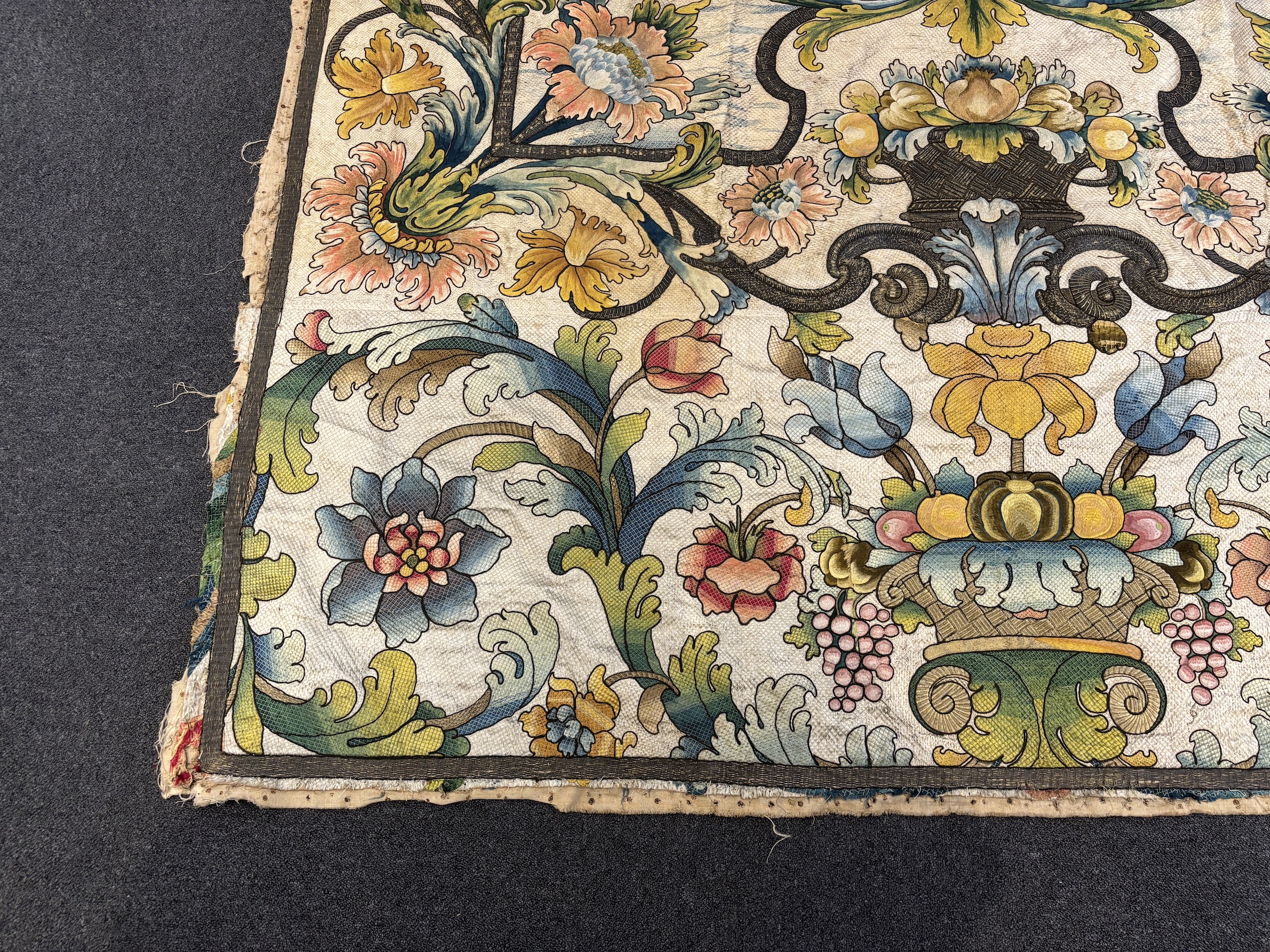 A large early 18th century possibly French polychrome and gold metallic silk embroidered wall hanging, with scrolling vine and floral border. The central motifs embroidered with an elaborate metallic thread cartouche fra